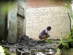 За углом дома молодая брюнетка на корточках мочится на скрытую камеру